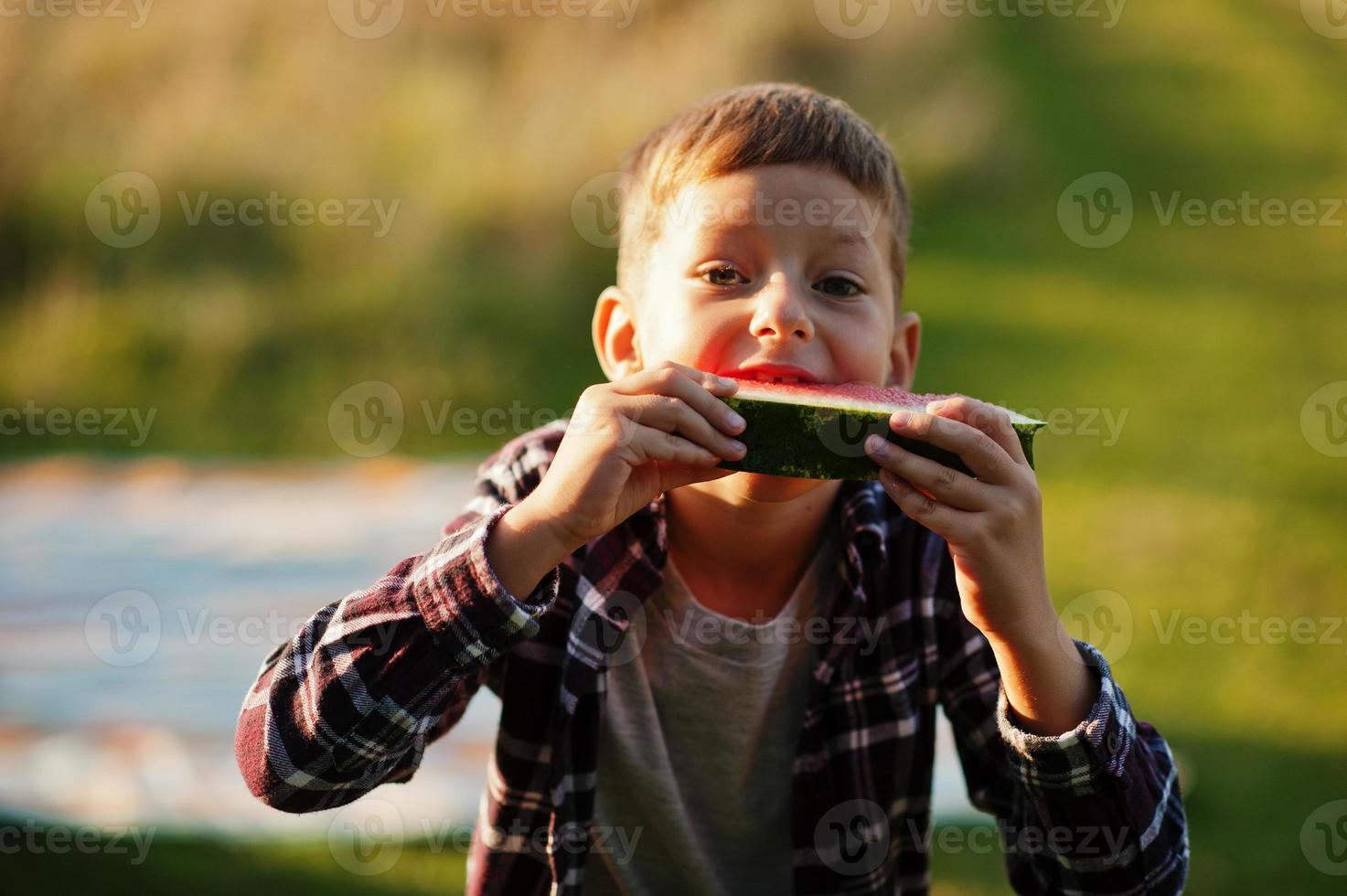 jongen draag geruit hemd eet watermeloen. foto
