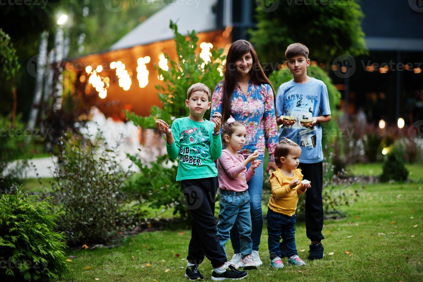 vier kinderen met moeder eten donuts in de avondtuin. lekker lekker donut eten. foto