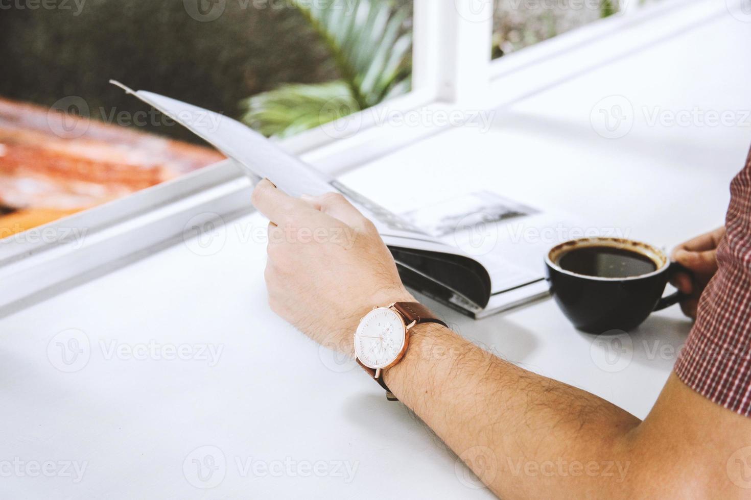 close-up van de hand van de man met een tijdschrift en een kopje koffie op witte tafel foto