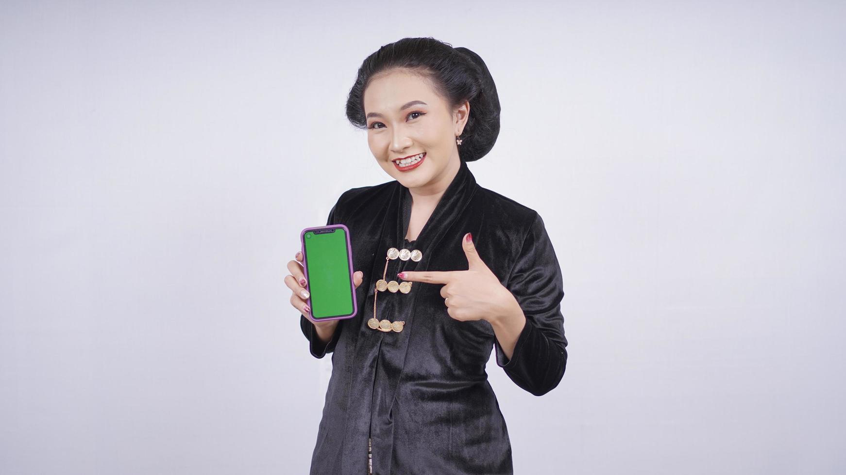 Aziatische schoonheid in kebaya die het smartphonescherm toont dat op witte achtergrond wordt geïsoleerd foto