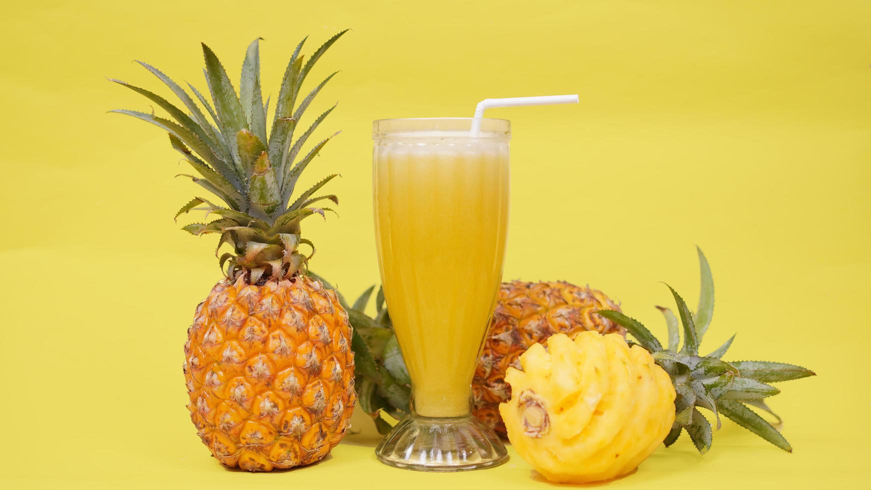 Ananasfruit en een glas sap dat op een gele achtergrond wordt geïsoleerd foto