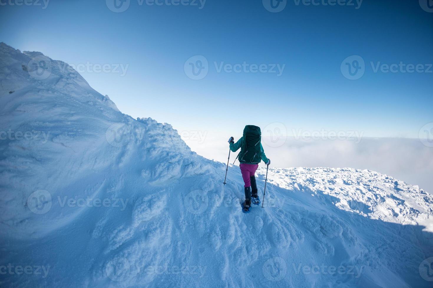 een vrouw met een rugzak op sneeuwschoenen beklimt een besneeuwde berg foto