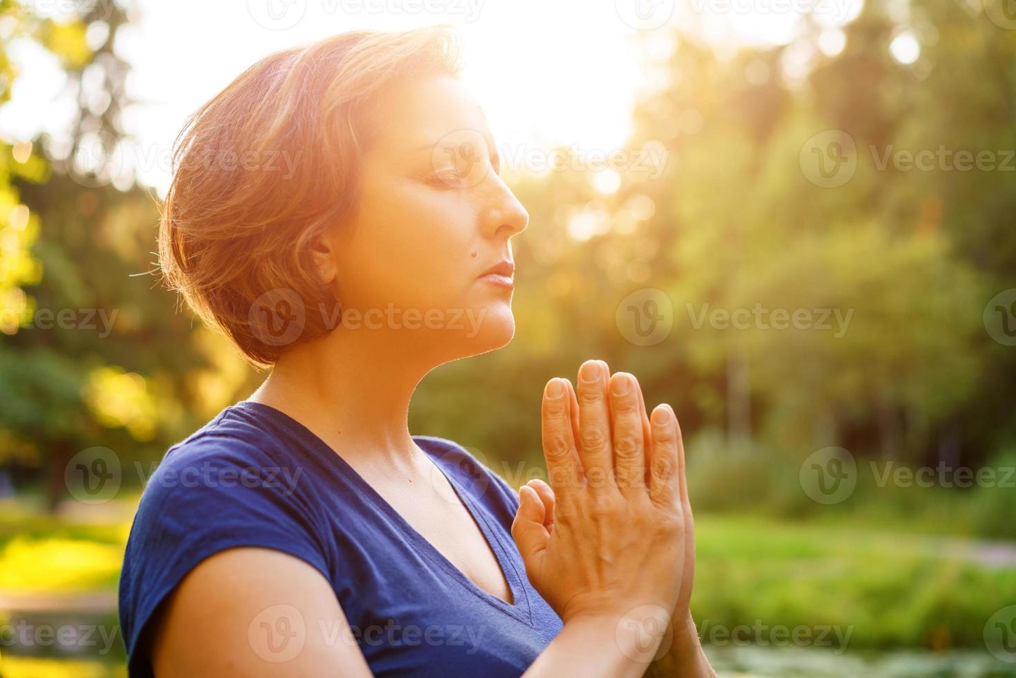vrouw staat met gevouwen handpalmen naar elkaar, tegen de achtergrond van de natuur foto