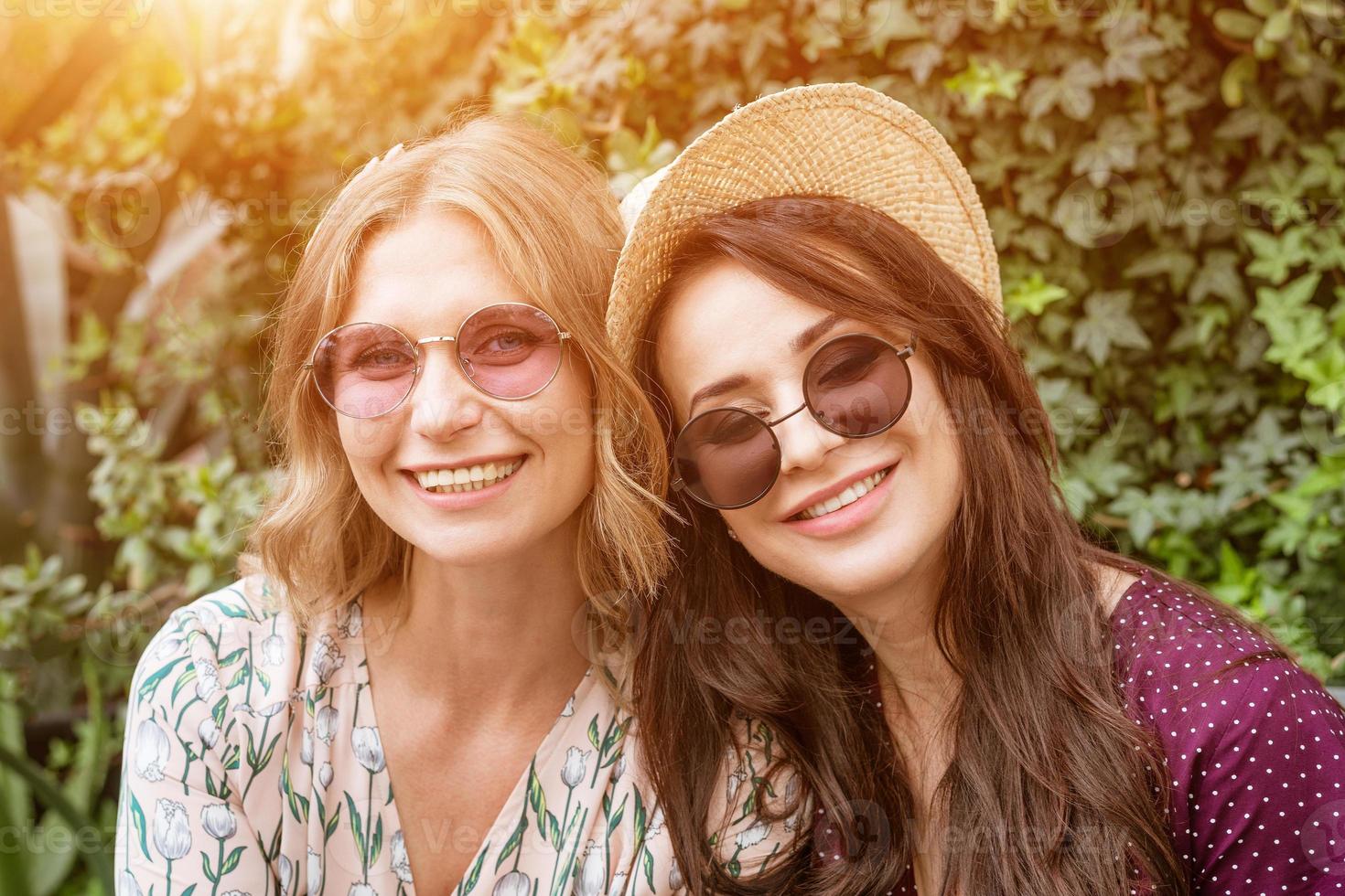 portret van twee vrolijke vrouwen in zonnebrillen en hoeden op een achtergrond van gebladerte foto