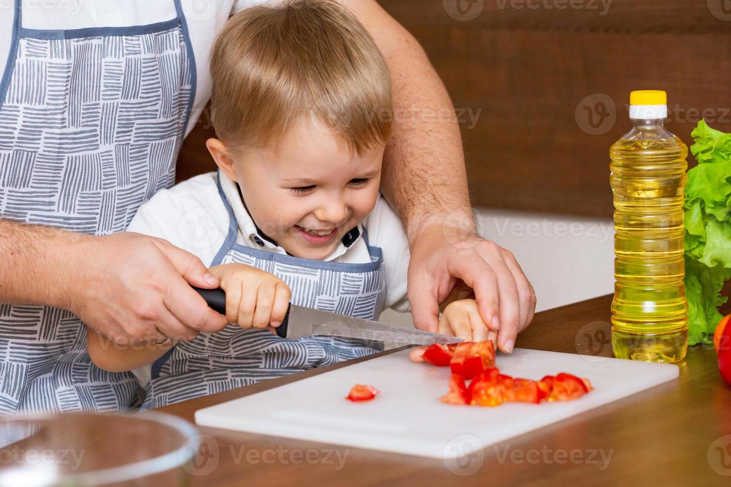 gelukkige vader leert zoon salade snijden in de keuken foto