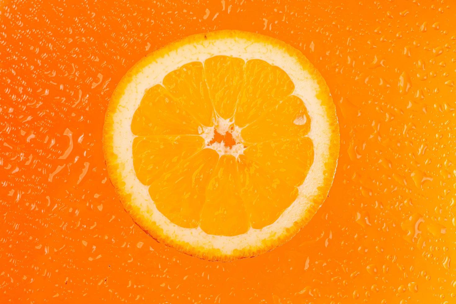 ronde sinaasappelschijfje met waterdruppels op oranje achtergrond foto