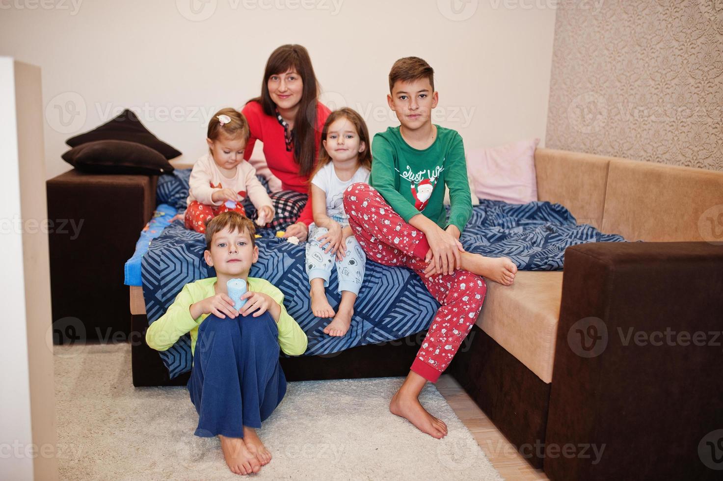 gelukkige grote familie heeft samen plezier in de slaapkamer. grote familie ochtend concept. moeder met vier kinderen draagt thuis een pyjama in bed. foto