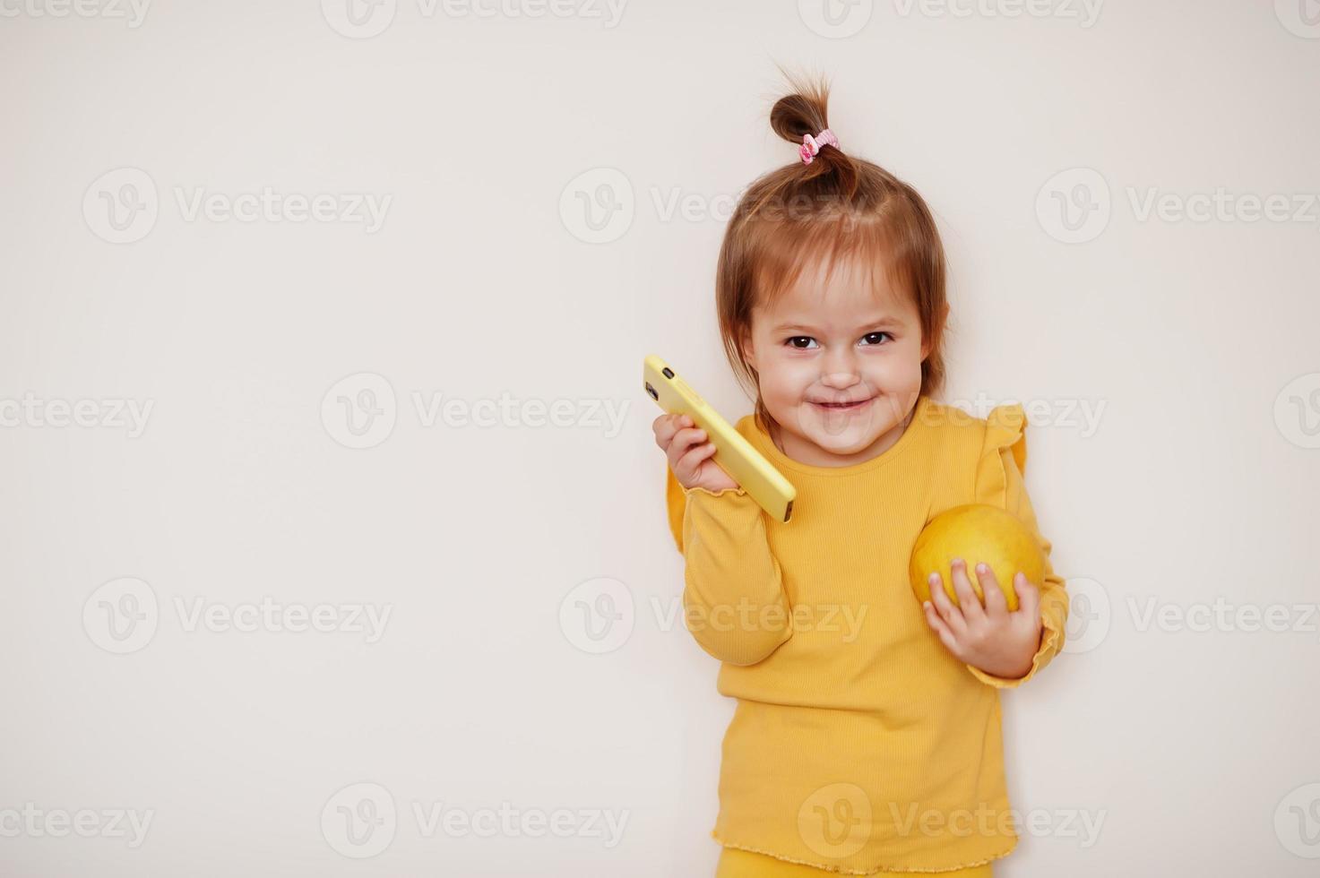 babymeisje in geel met citroen en mobiele telefoon, geïsoleerde achtergrond. foto