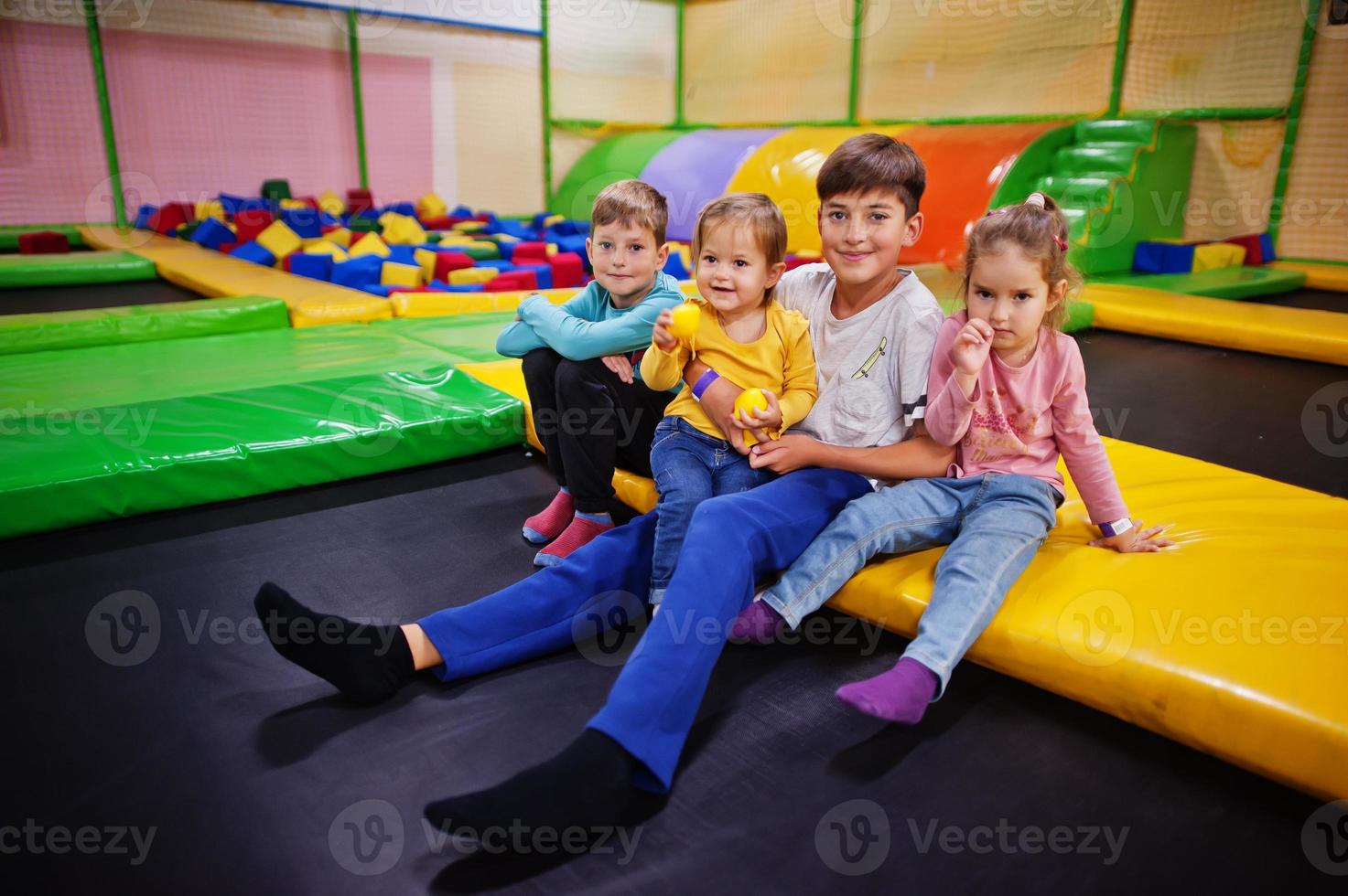 kinderen spelen in het overdekte speelcentrum en zitten op een trampoline. groot gezin met vier kinderen. foto