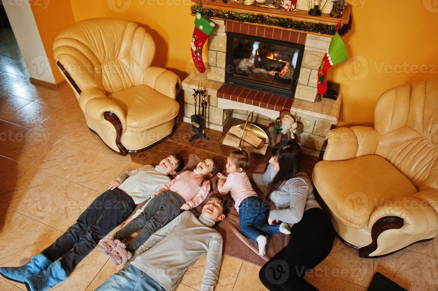 gelukkige jonge grote familie bij een open haard in warme woonkamer op winterdag. moeder met vier kinderen thuis. foto