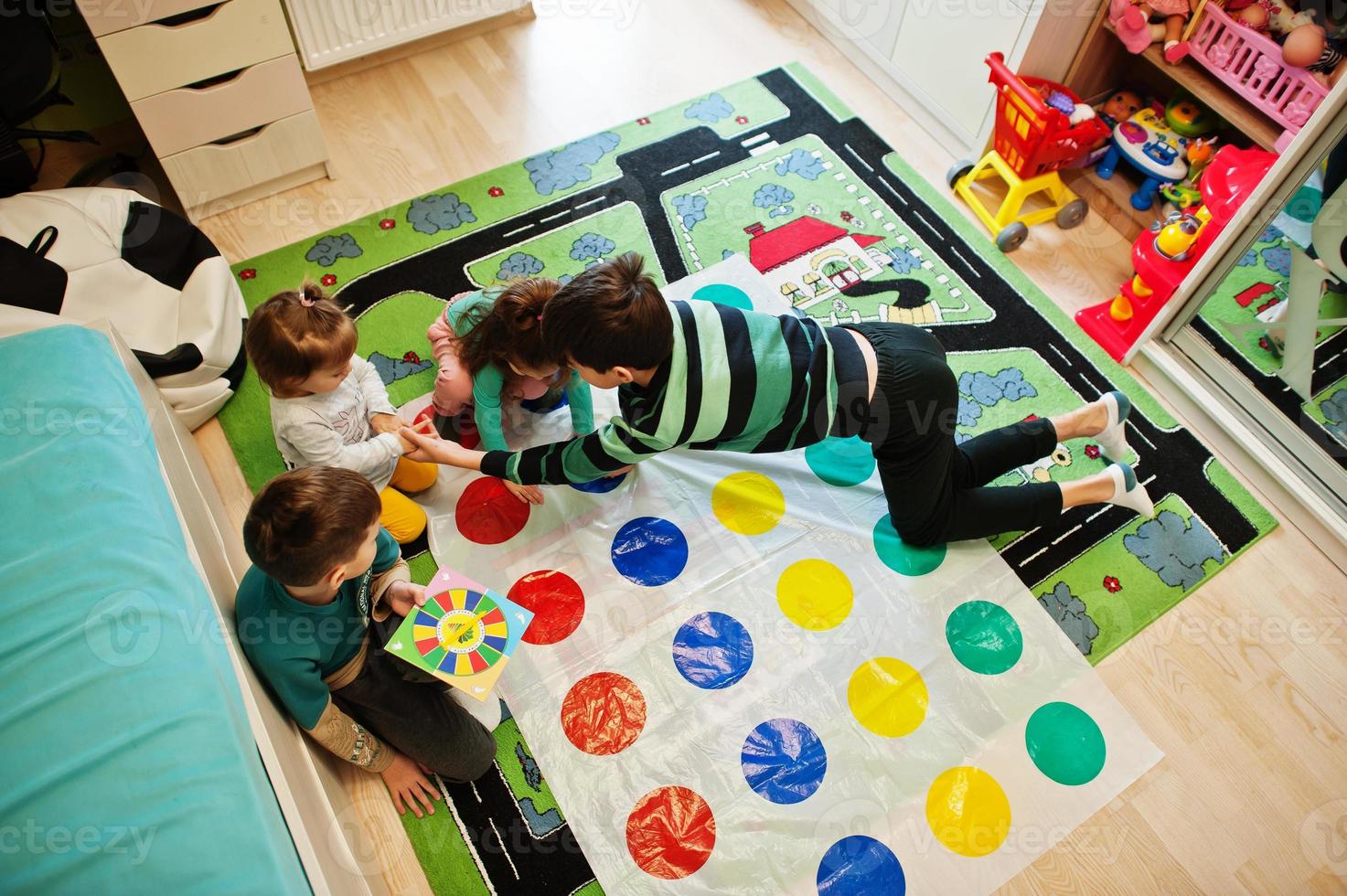 gelukkige familie die samen plezier heeft, vier kinderen die thuis een twister-spel spelen. foto