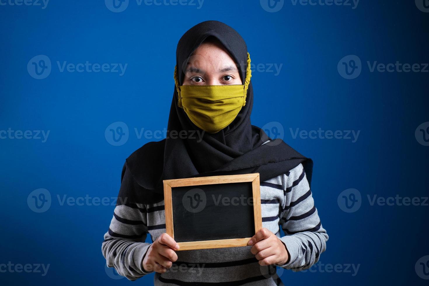 portret van een jonge aziatische vrouw die een beschermend masker draagt tegen het coronavirus, met een klein schoolbord foto