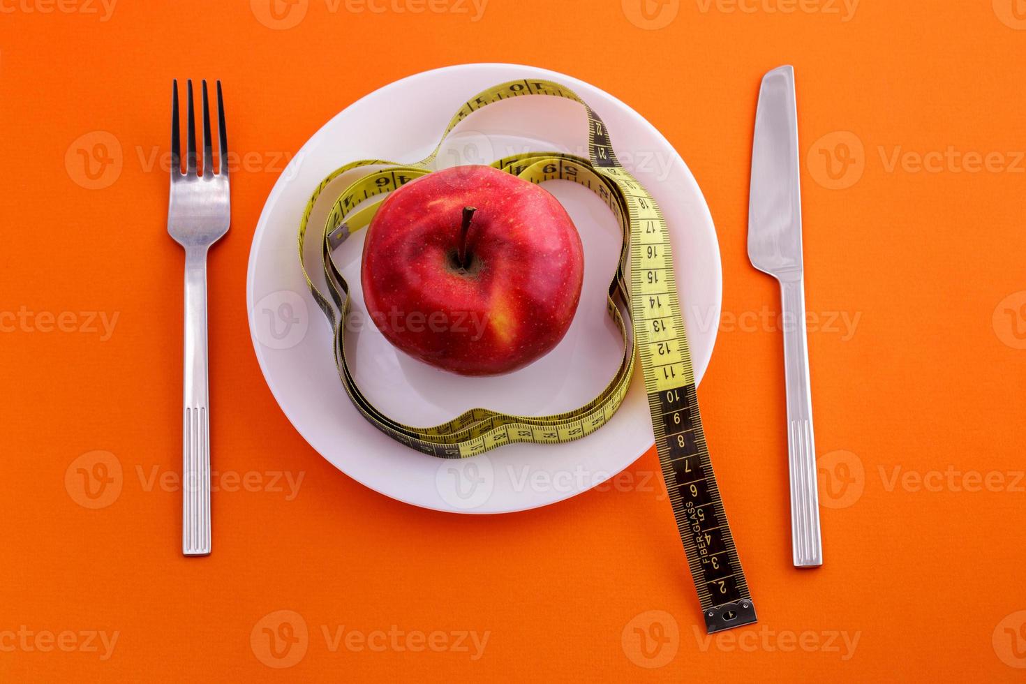 rode appel op plaat met meetlint, mes en vork op een oranje achtergrond foto