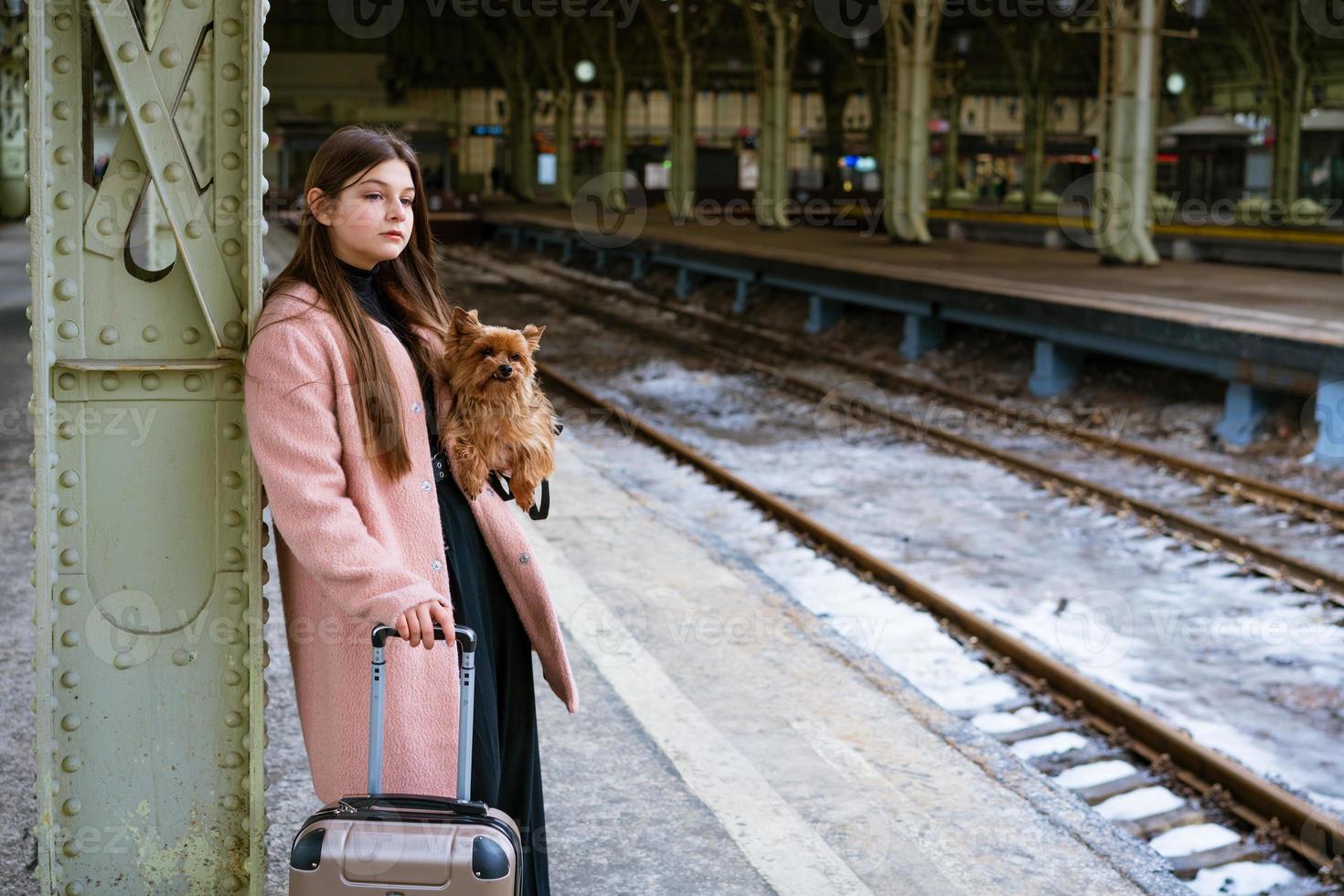 mooie jonge casual toeristenvrouw met hond en koffer die op trein wacht foto