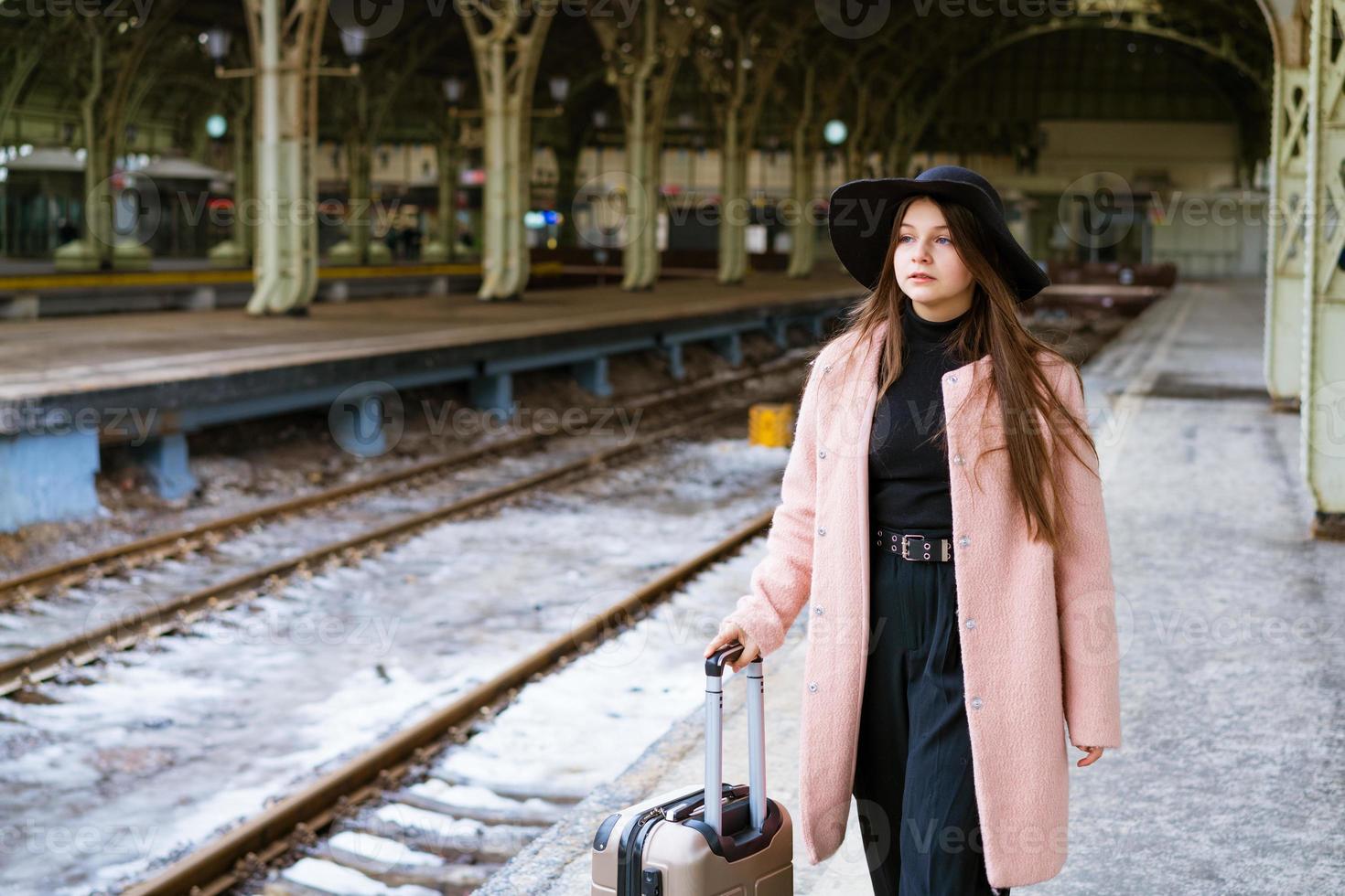 jonge vrouw met koffer op perron van station. reizigersmeisje te wachten foto