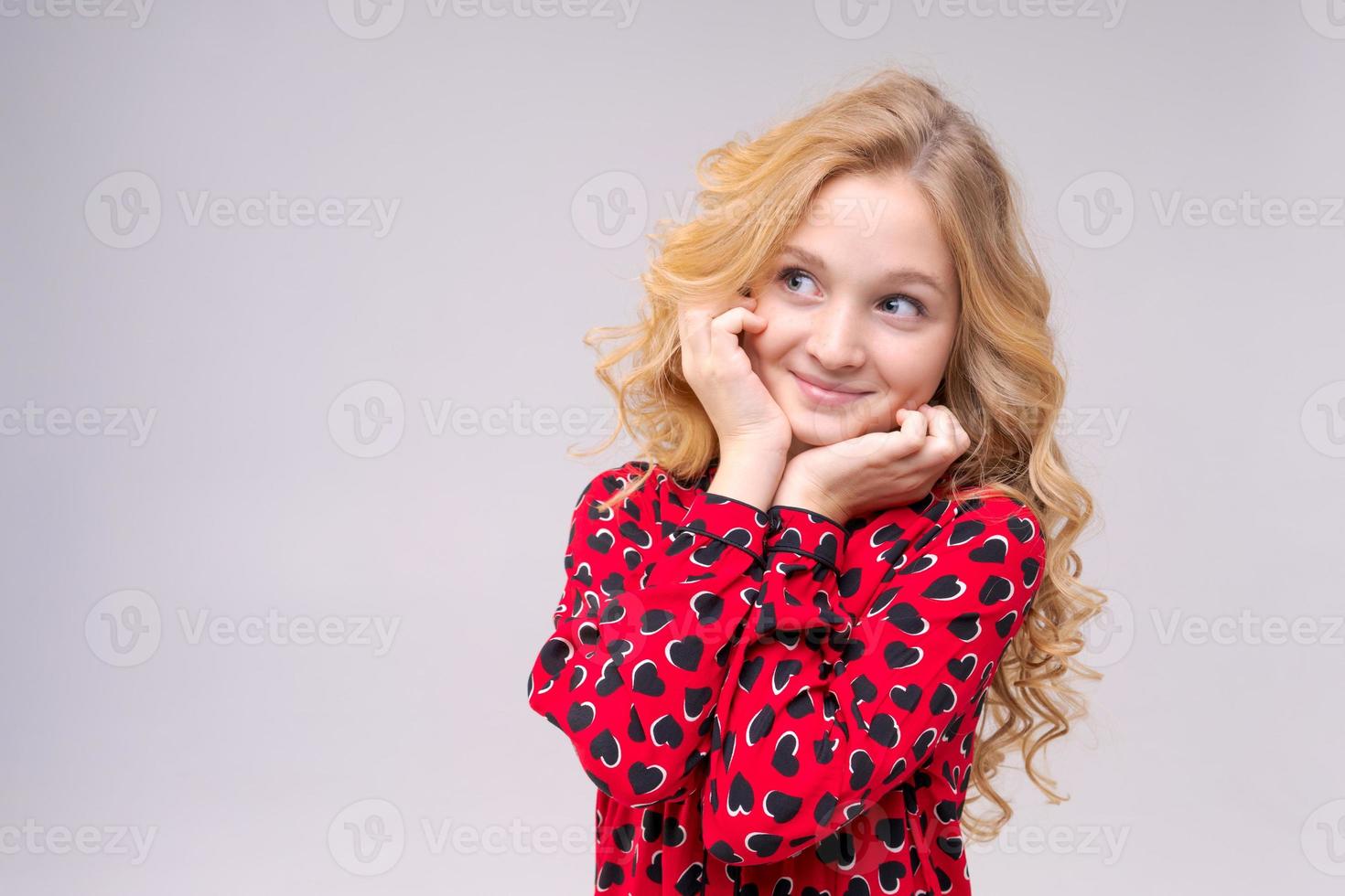 klein grappig kindmeisje van 8 jaar oud draagt een rode jurk met lang golvend haar foto