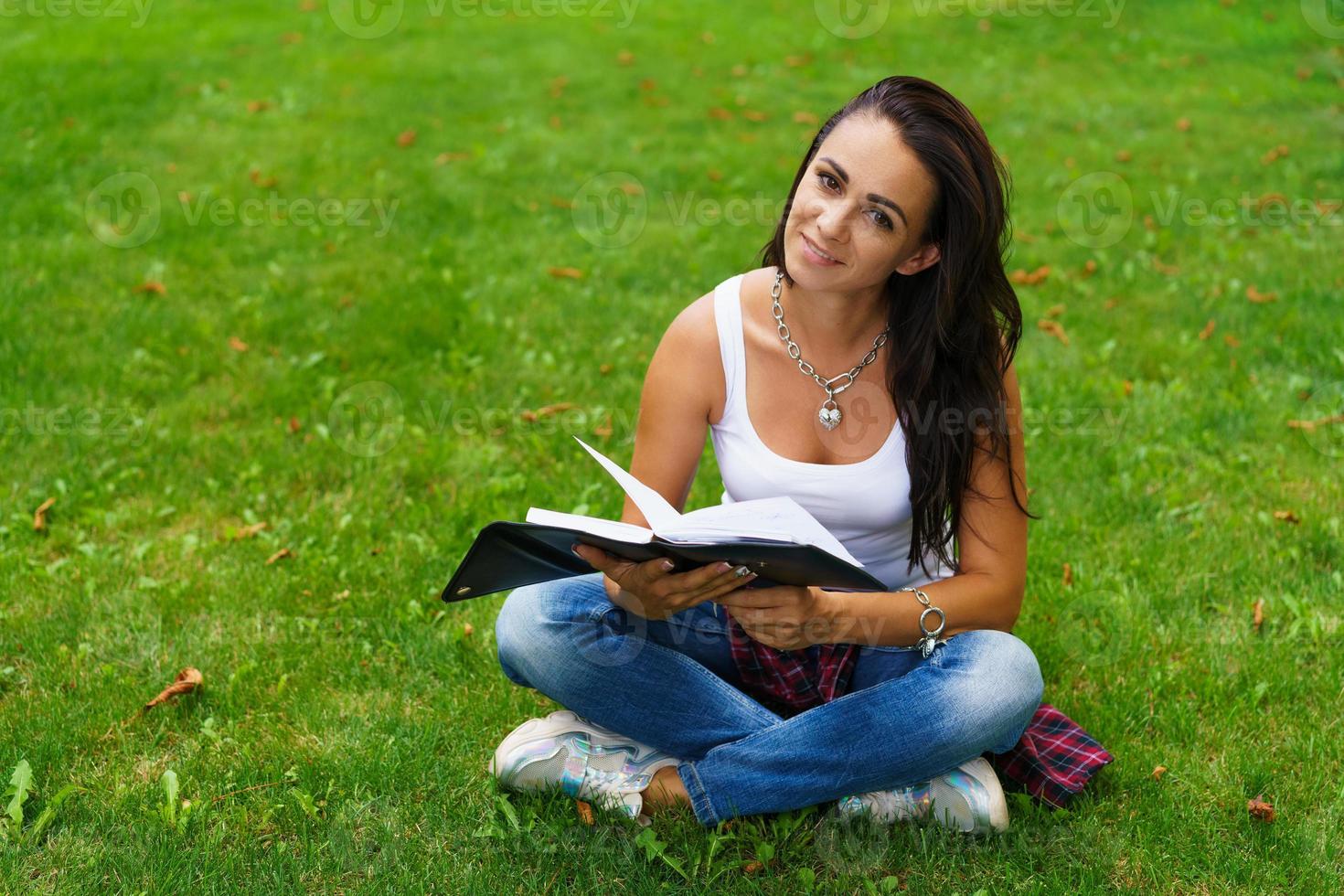 mooi meisje in vrijetijdskleding zit op het gras in het universiteitspark met foto