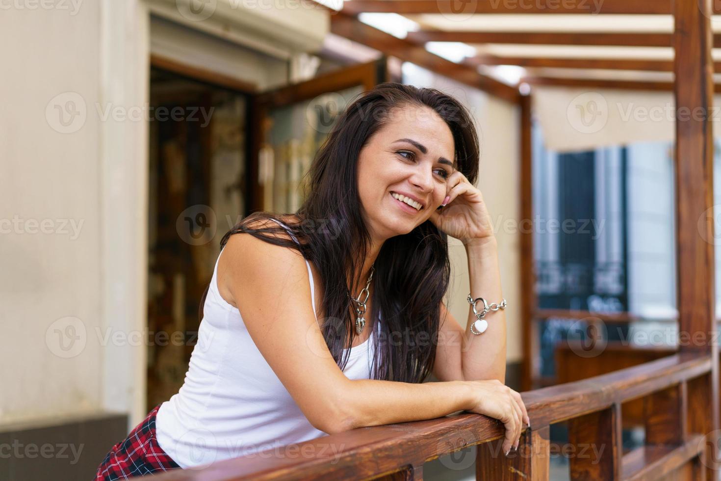 jonge blanke vrouw lacht staande op de veranda bij de deur van de winkel in casual foto