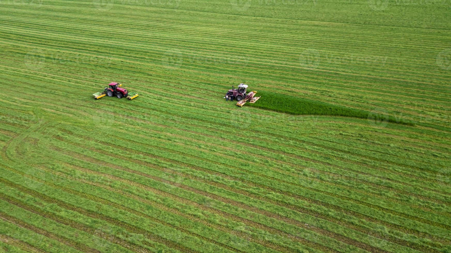 twee tractoren maaien het gras op een groen veld vanuit de lucht foto