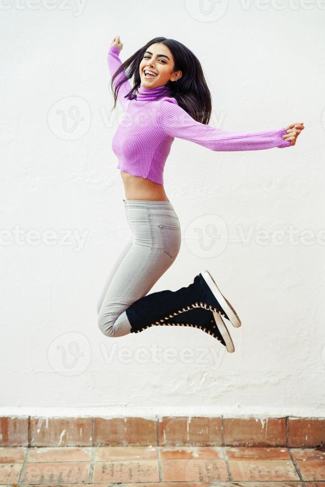 gelukkige Perzische vrouw die buiten op witte muur springt foto