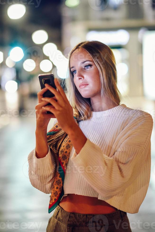 vrouw die 's nachts op straat foto's maakt met smartphone foto