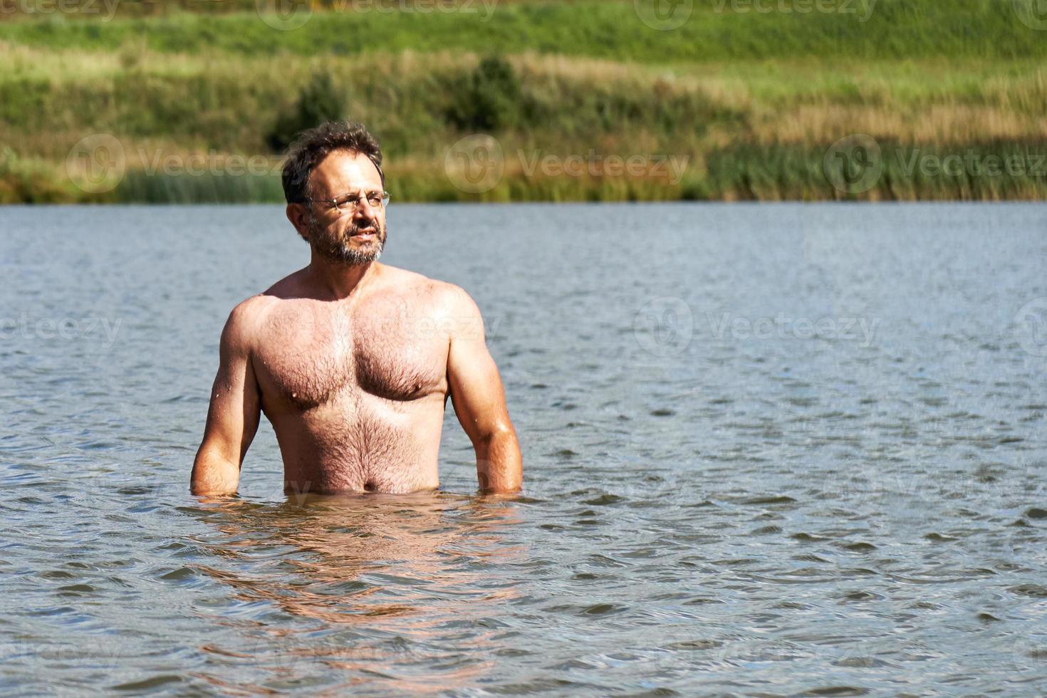 sportieve man van middelbare leeftijd baadt in het kleine meer in de voorsteden in de zomer foto