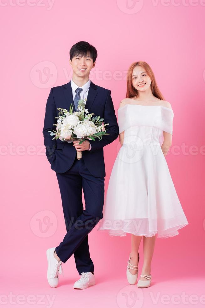 jonge Aziatische bruid en bruidegom poseren op roze achtergrond foto