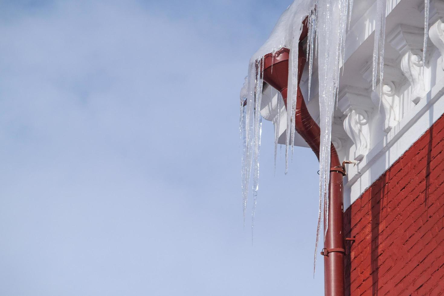 besneeuwd dak van een hoog bakstenen huis met grote gevaarlijke ijspegels. foto