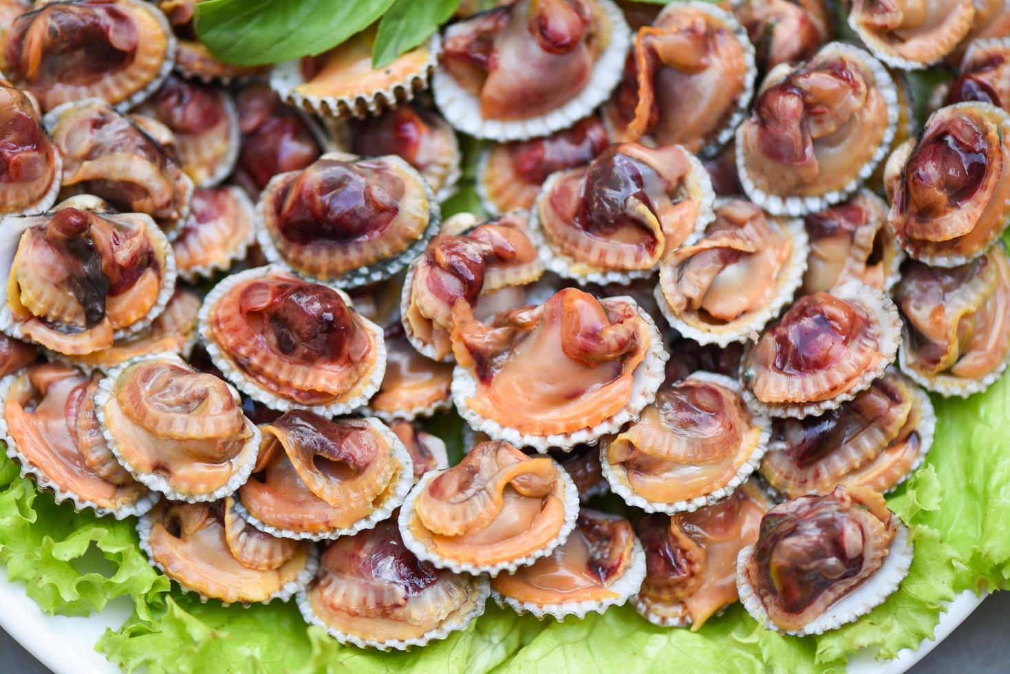 gepelde kokkels met zeevruchtensaus en groentesalade sla op plaat houten achtergrond, verse rauwe schelpdieren bloed kokkel oceaan gastronomische zeevruchten in het restaurant, zeeschelpen eten foto