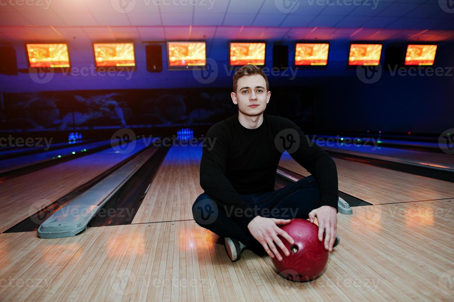 jonge man met een bowlingbal zittend tegen bowlingbanen met ultraviolet licht. foto
