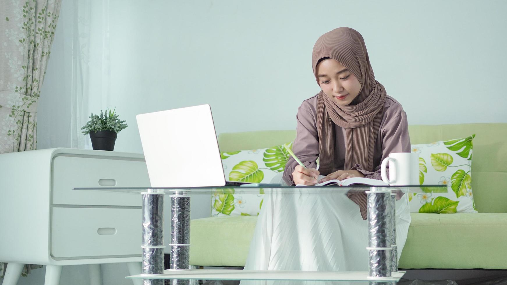 mooie aziatische vrouw in hijab die vanuit huis werkt en aantekeningen maakt foto