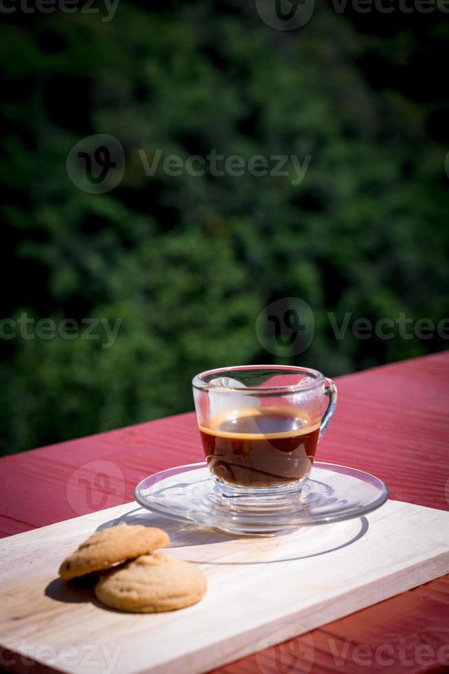 espresso of zwarte koffie geserveerd met boter en vanillekoekjes op houten tafel met groene natuurlijke achtergrond. energiedrank in het ochtendconcept. foto