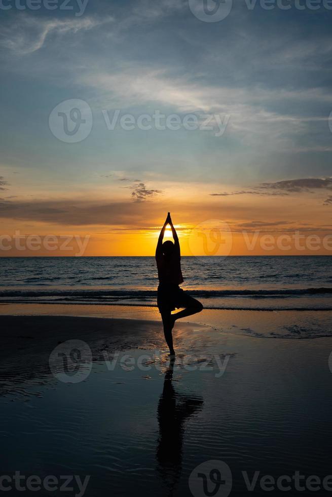 silhouet van de mens mediteren op het strand bij zonsondergang foto