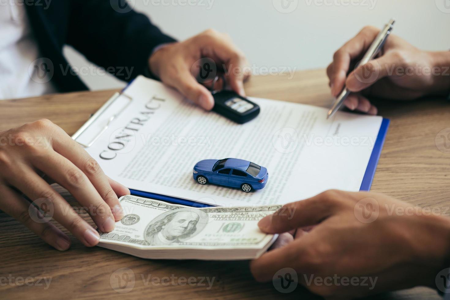 kopers van nieuwe auto's tekenen een contract met een autoverkoper in de showroom op de dag van ontvangst van de auto en het overhandigen van contant geld aan de medewerker. foto