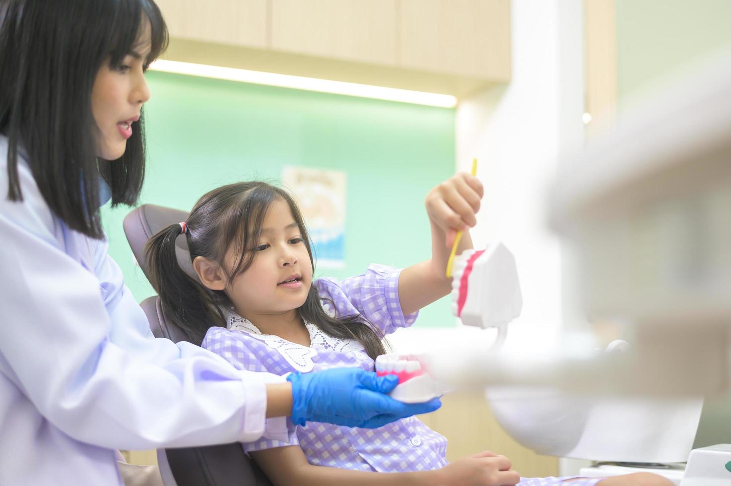 vrouwelijke tandarts die laat zien hoe je tanden poetst aan een klein meisje in de tandheelkundige kliniek, tandencontrole en gezond tandenconcept foto