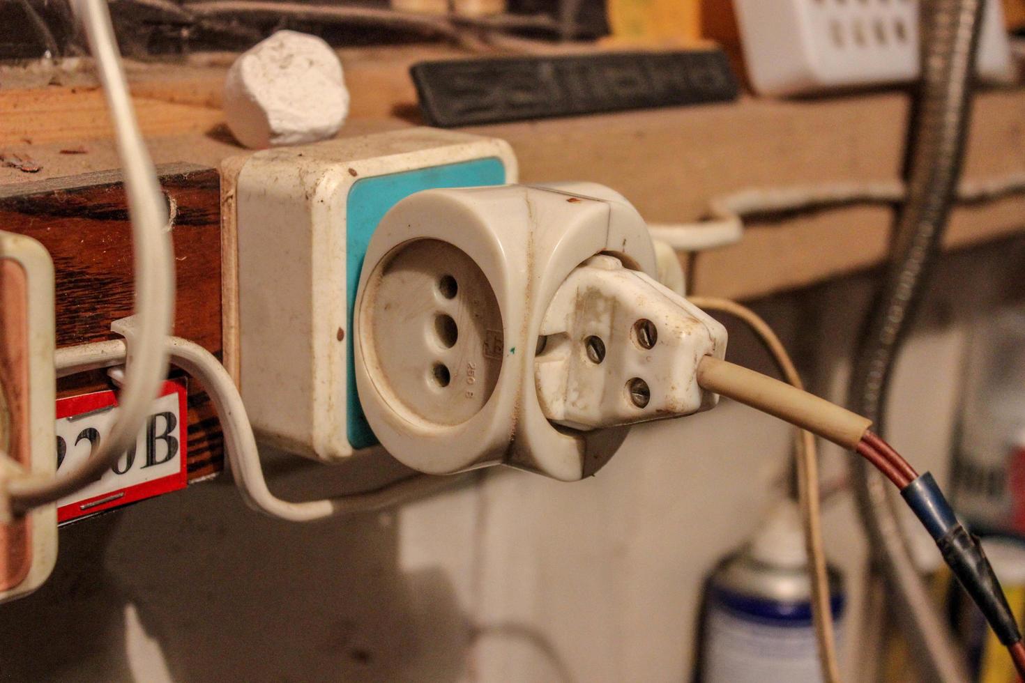 een oude elektrische stekker met een teruggewikkelde elektrische tape aangesloten op een stopcontact. elektrische bedrading in de garage foto