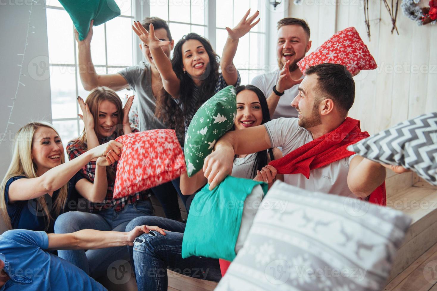 gekke jonge beste vrienden die thuis met kussens vechten. gemengd ras groep mensen. conceptentertainment en lifestyle foto