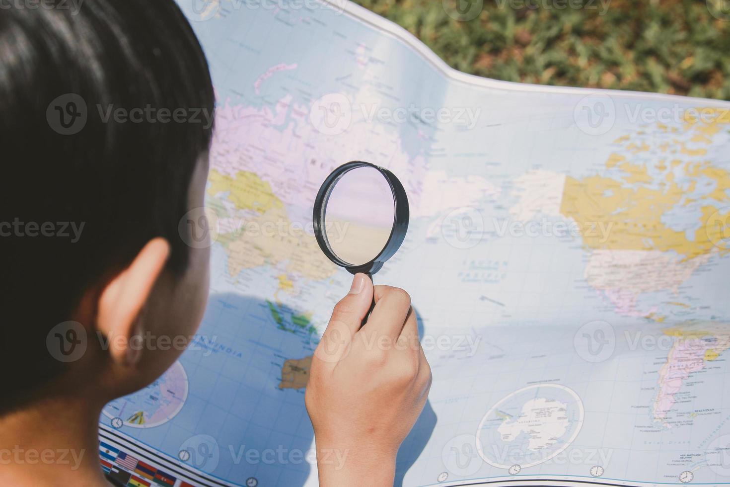 een jongen die locatie op de wereldkaart zoekt met behulp van vergrootglas foto