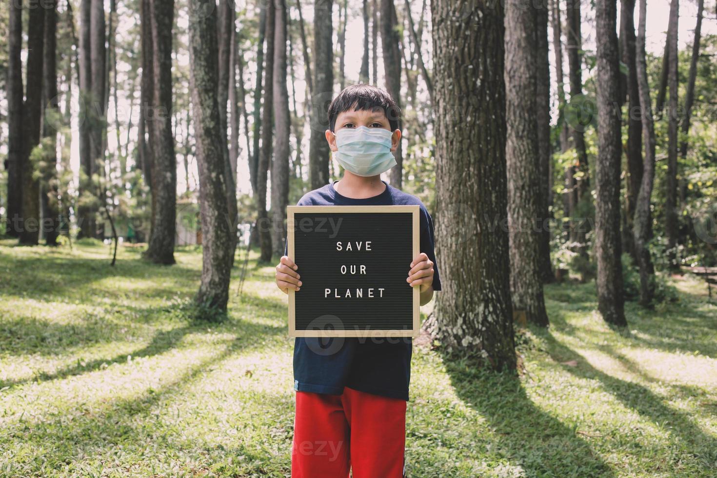 een jongen die een citaat op een letterbord laat zien, zegt onze planeet te redden met bos op de achtergrond, het concept van de aardedag foto