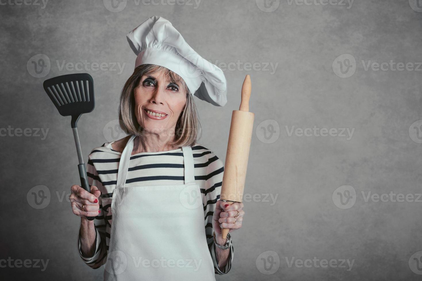 lachende senior vrouw met kok hoed en deegroller en spatel foto