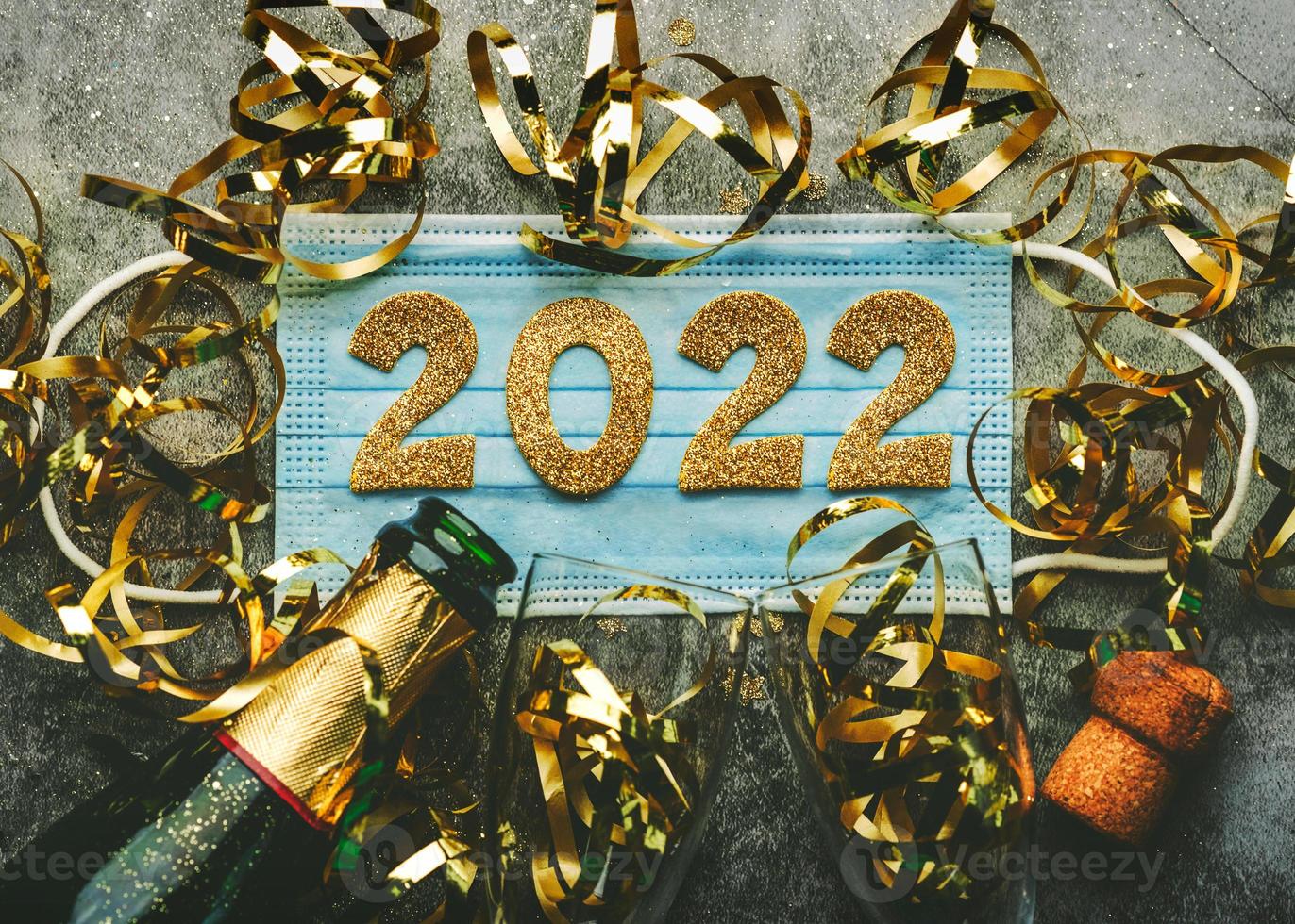 oudejaarsavond viering concept background.medical masker met de nummers 2022 en champagnefles met glazen .covid-19 nieuwjaarsconcept op grijze achtergrond foto