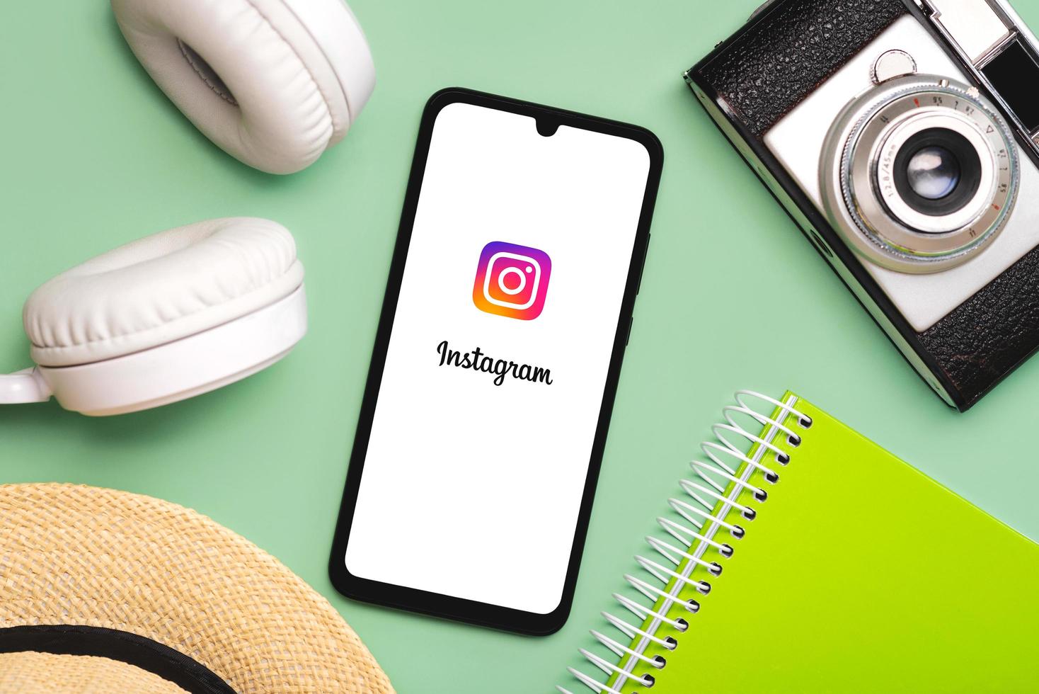 instagram-toepassingspictogram op wit scherm van smartphone met witte draadloze hoofdtelefoon, vintage fotocamera, hoed en notebook foto