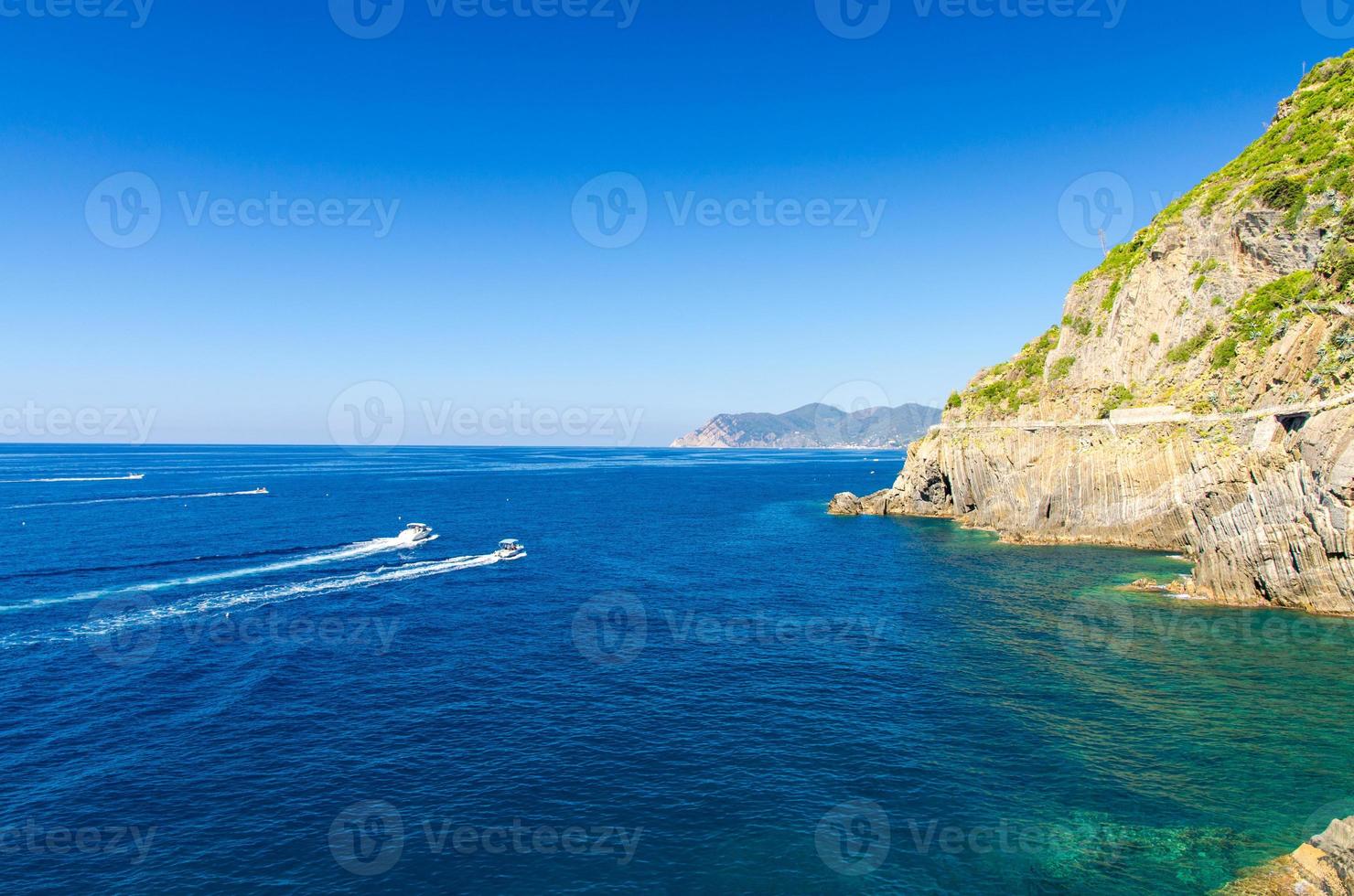 twee jachten boten varen op het water van de Ligurische en Middellandse Zee in de buurt van de kustlijn van de riviera di levante van het nationaal park Cinque Terre kust met blauwe lucht kopieerruimte, het dorp Riomaggiore, Ligurië, Italië foto