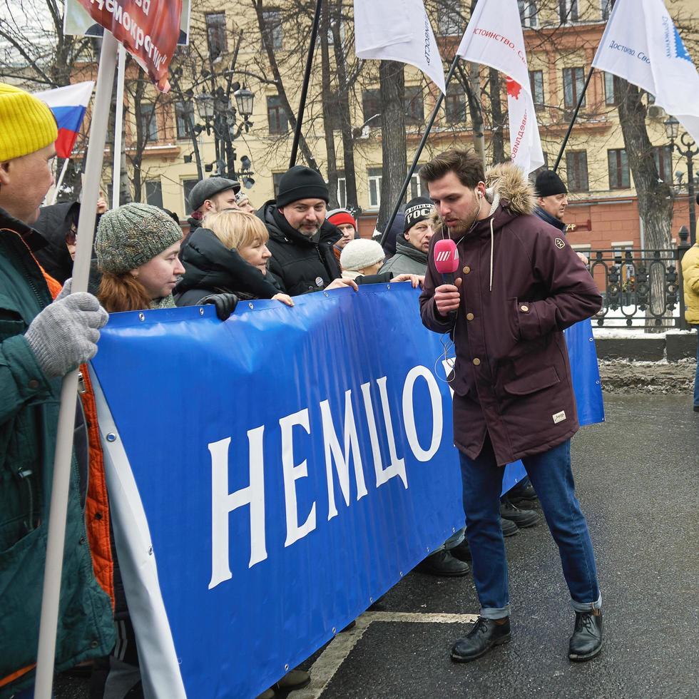 Moskou, Rusland - 24 februari 2019. Nemtsov Memorial March. verslaggever van de Russische tv-regenzender Aleksei Korostelev interviewt demonstranten met een politiek spandoek foto