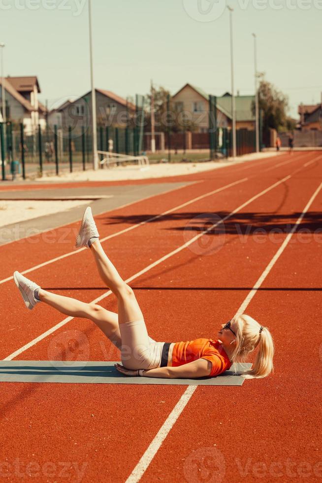 jonge blonde schudt buikspieren op een sportmat op straat foto