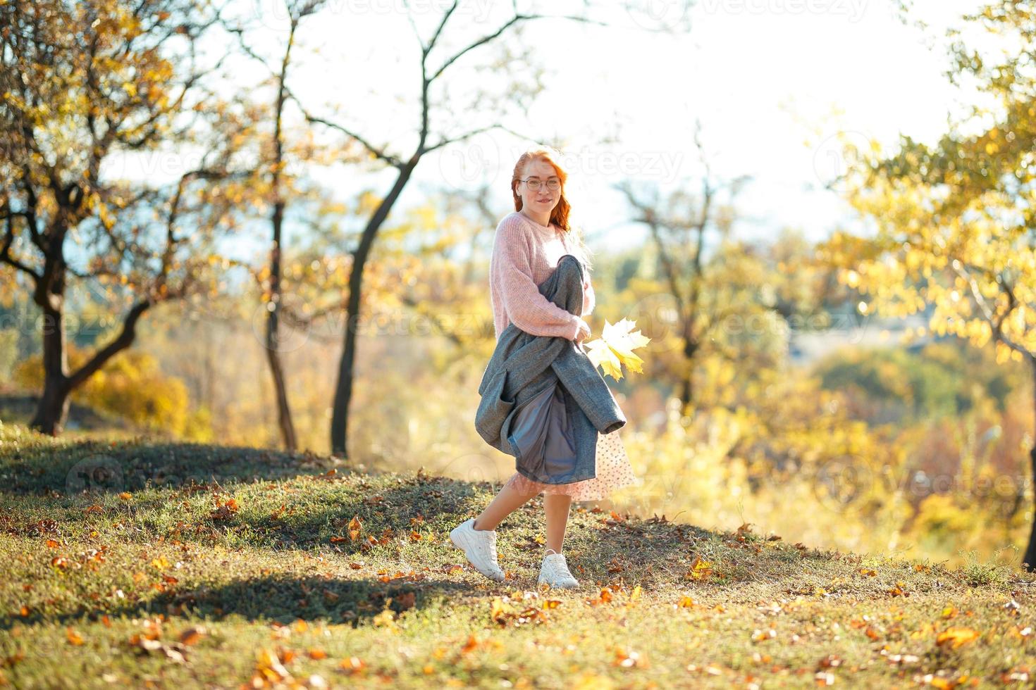 portretten van een charmant roodharig meisje met een schattig gezicht. meisje poseren in herfst park in een trui en een koraalkleurige rok. het meisje heeft een geweldige bui foto