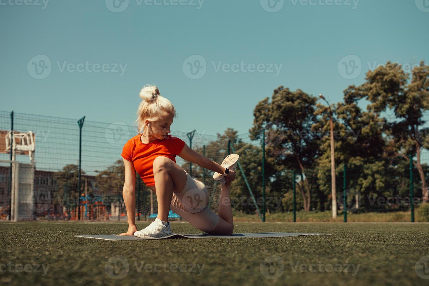 mooie blonde doet strekken op het gazon van een voetbalveld foto