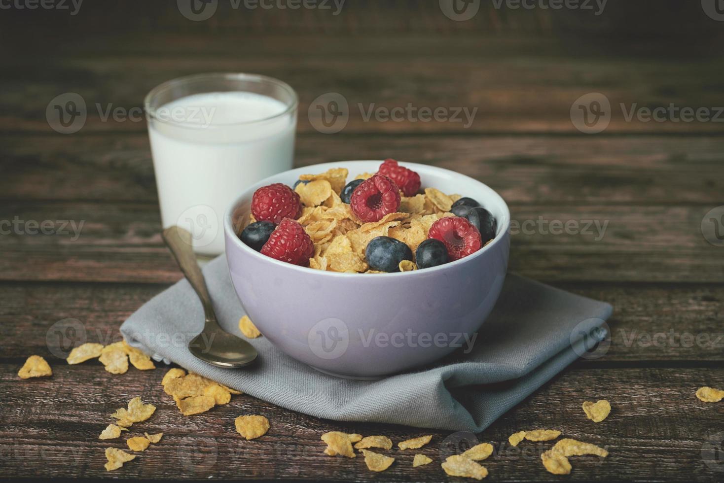 kom cornflakes, bosbessen, frambozen en glas melk foto