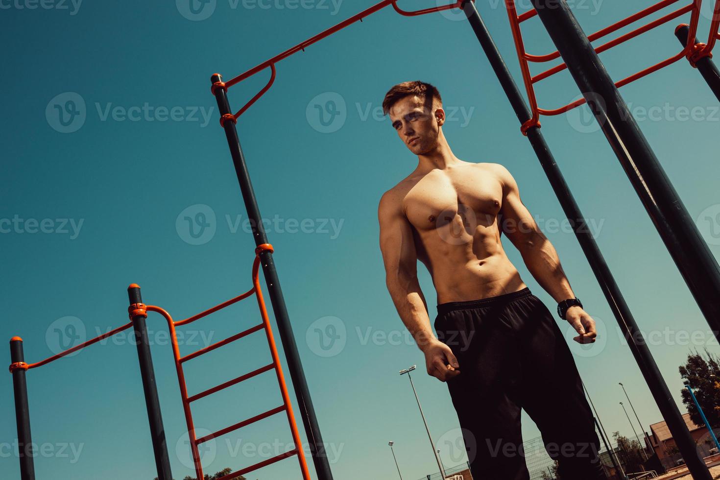 man met een mooi atletisch lichaam die poseert terwijl hij naast de horizontale balken staat foto