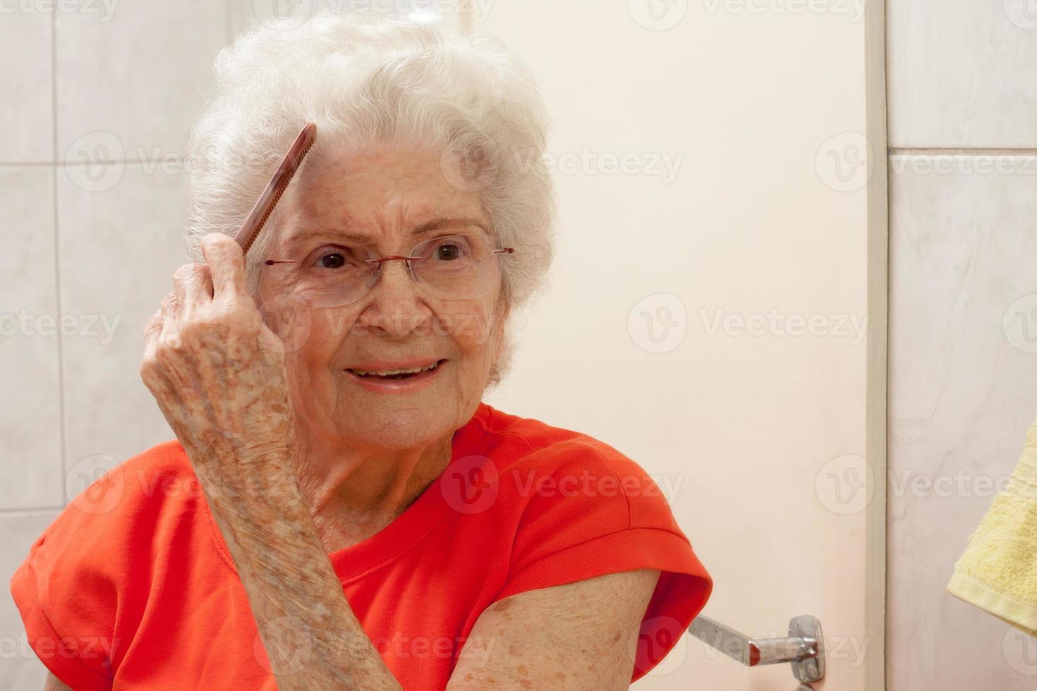 oudere dame die haar haar kamt voor een spiegel in de badkamer foto
